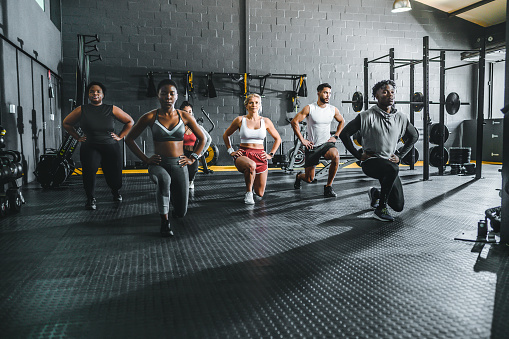 Multiracial group of athletes with arms on hips, training on lunges in gym