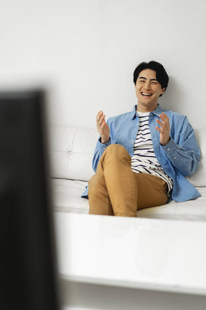istock Happy Japanese man sitting on sofa and watching television 1494139352