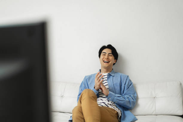 istock Happy Japanese man sitting on sofa and watching television 1494139353