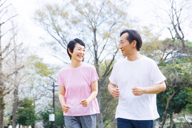 Pareja japonesa madura en ropa deportiva trotando en un parque - foto de stock