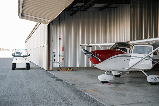 An environmental showcase of airplane hangar and its surroundings: one light aircraft and a golf cart is in frame.
