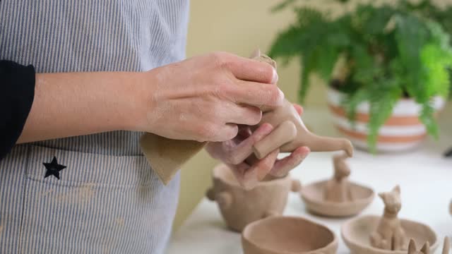 woman sculpts a figurine of a dsnosaur from clay by hands, closeup in artistic studio