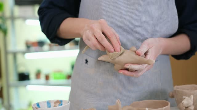 woman sculpts a figurine of a dsnosaur from clay by hands, closeup in artistic studio