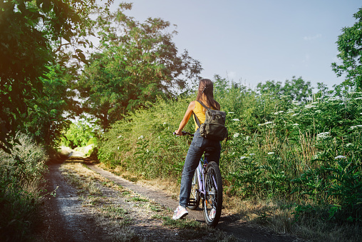 Urban biking woman riding bicycle in city park.Girl on bicycle walks in sunny warm day in the park.Young Woman Riding Bicycle on Free Road in the Forest at Hot Summer Day.Healthy Lifestyle Concept.Girl enjoying bike ride on her way warm summer day.