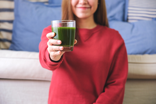 Closeup image of a young woman holding and showing a glass of kale smoothies