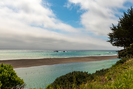 View of the Gualala River and Paciic Ocean from the Bluff Trail in Gualala, California, USA, featuring large partly cloudy sky space for copy