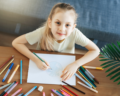 Child girl drawing with colorful pencils at home. Ecology concept, painting earth.