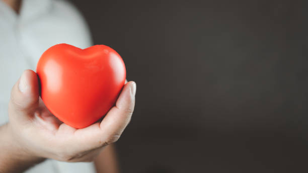 istock Man holding a red heart shape while standing with black background with space for text. 1494178320