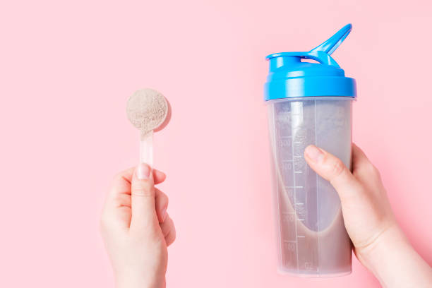 istock Female hand holds shaker with protein shake and scoop on pink background. 1494184109