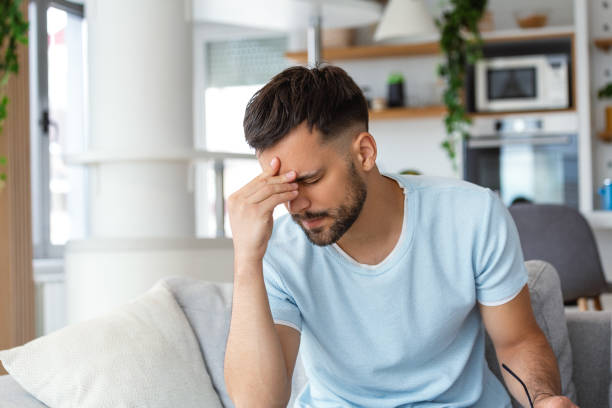istock Feeling stressed. Frustrated handsome young man touching his head and keeping eyes closed while sitting on the couch at home 1494197025
