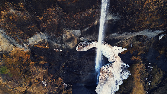 Drone shot of wild foss a sidu cascade, river flow running off frozen cliffs. Icelandic beautiful waterfall in iceland flowing down off mountains, fantastic panoramic landscape. Slow motion.