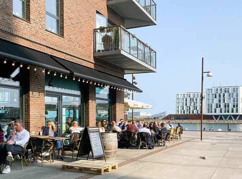The photo was taken at a sidewalk Cafe on May 26th, 2023 in a new fashionable district by the sea in Nordhavn, Copenhagen, Denmark. Residential apartments are mixed with office buildings and business making the area  attractive and very much alive. Balcony of Luxury apartments can be seen above the Cafe.
