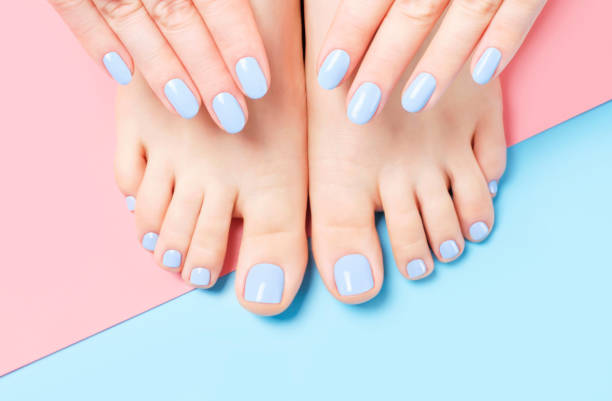Female hands and feet with light blue manicure and pedicure on a blue and pink background top view close-up. stock photo