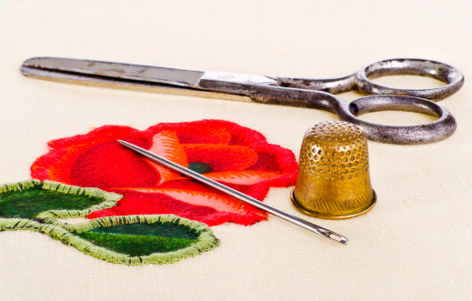 old scissors, a thimble and a needle lying on needlework. The image collected from five shots to increase the zone of focus