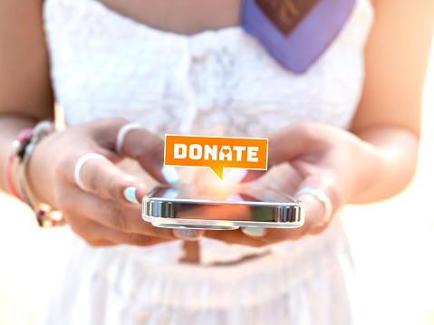 Close-up donate icon in bubble speech symbol appear on smart mobile phone in stylish woman's hands in white dress. Donation online on website or application by cell phone concept.