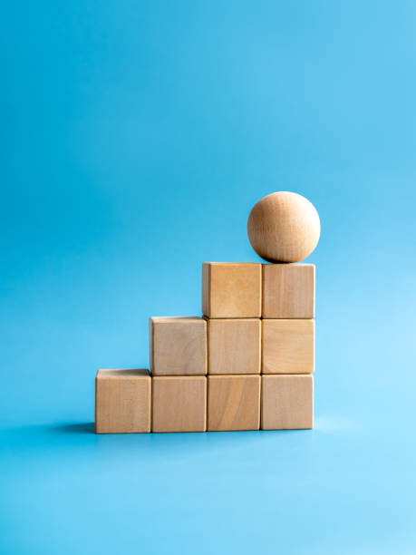 istock Wooden sphere on top of wood cube block bar graph chart steps on blue background, vertical style. Business growth process, trend, development, change, goal and success, economic improvement concepts. 1494203082