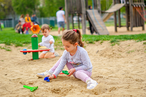 Kids playing at park - Little girls sitting down in sand playing joyfully