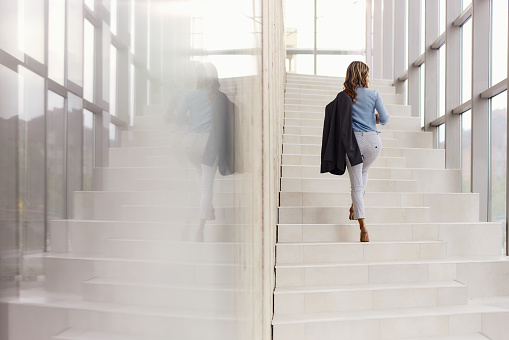 Rear view of a female entrepreneur moving up the stairs in a hallway of an office building. Copy space.