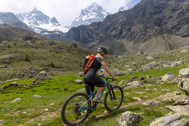 young woman rides e-bicycle up mountain trail - on top of mountain peak success cold imagens e fotografias de stock