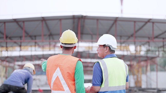 Engineer or supervisor and or foreman have expertise wearing safety uniform, standing together discuss process in construction site of buildings or housing projects. Employee is working in real estate construction industry.