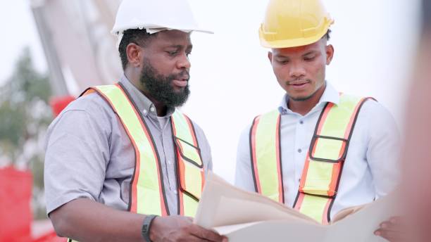 istock Civil engineer working inspection at construction site. Contractor and foreman discuses about details of building design and inspect construction progress in blueprint. Two engineers wearing safety uniform and helmets walking in housing construction site. 1494226357