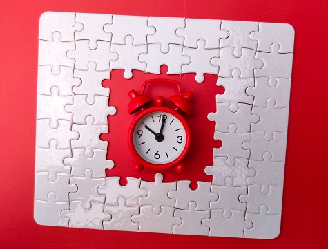 A vibrant red alarm clock sits nestled within a square shaped jigsaw puzzle piece