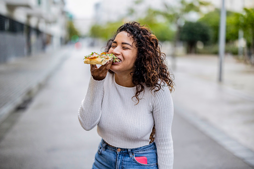 overweight woman eating pizza in the city, cuvy hispanic girl happy while eating rich italian food