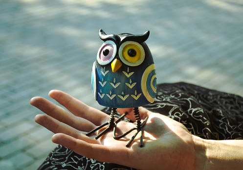 A funny toy of a cute and surprised owl stands on the palm of a female hand