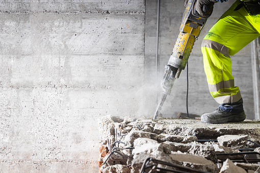 Construction worker using heavy-duty jackhammer tool and breaking reinforced concrete.