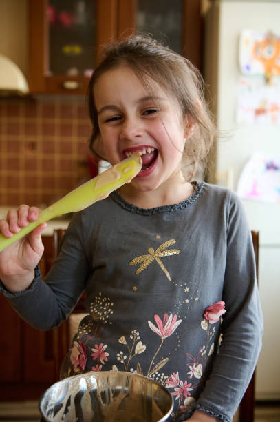 istock Mischievous child girl tastes melted Belgian chocolate, standing at kitchen table, smiling slyly looking at the camera. 1494236382