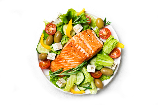 Fresh greek vegetable salad with green olives and feta cheese and grilled salmon fish steak isolated on white background. Healthy balanced food concept. Greek mediterranean food.