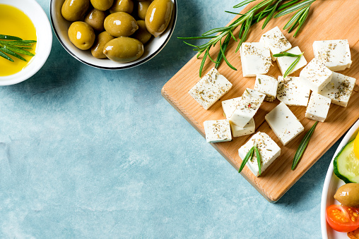 Healthy ingredients for cooking salad - Feta cheese, olives and olive oil. Mediterranean greek food. Chopped Goat feta cheese with rosemary herbs, copy space.