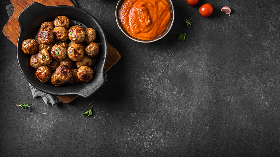 Fryed meatballs on black background, top view, copy space. Beef roasted meatballs and tomato sauce ready for eat.