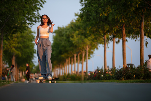 Young skater woman in public park at sunset.
