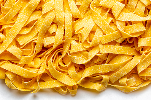 Homemade fresh, uncooked tagliatelle or fettuccine background,  is a traditional type of italian pasta.  Long, flat ribbons traditionally made of egg and flour. Directly above.