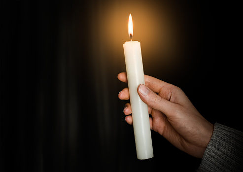 female hand holding a burning candle on a dark background. power outage