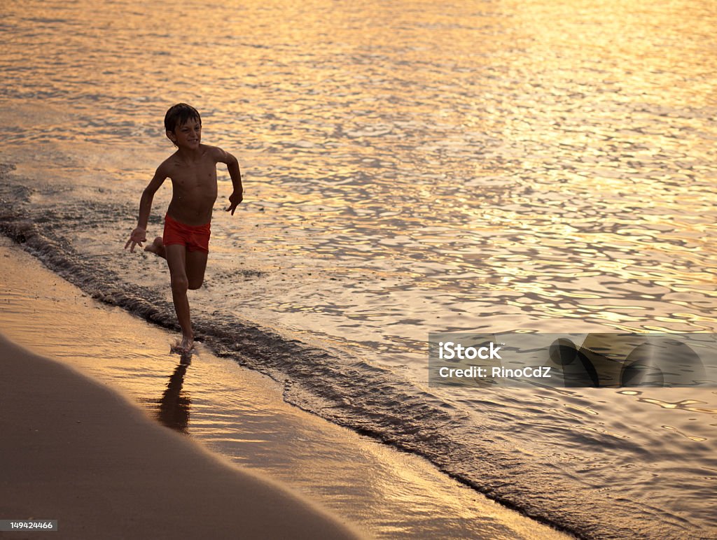 Running chłopiec na Seashore o zachodzie słońca - Zbiór zdjęć royalty-free (Biegać)