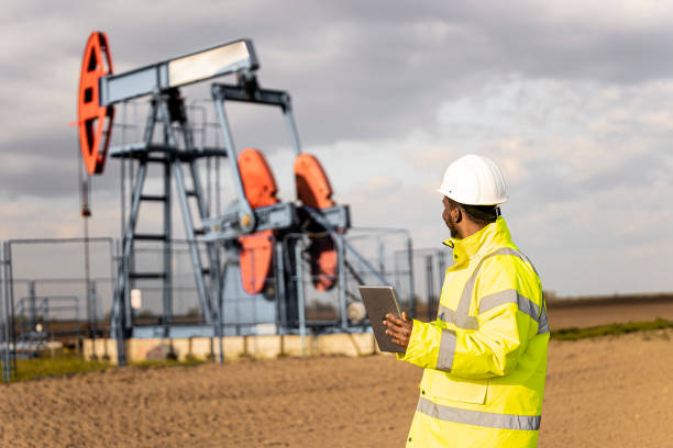 油田エンジニアの整備士が石油掘削装置の掘削作業を監視し、デジタルタブレットを保持します。 - oil industry digital tablet manual worker mining ストックフォトと画像