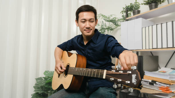 istock Young joyful asian handsome man playing  guitar at home. 1494250747