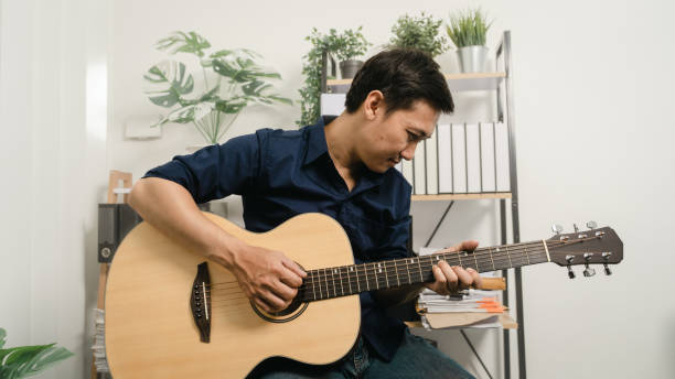 istock Young joyful asian handsome man playing  guitar at home. 1494250755
