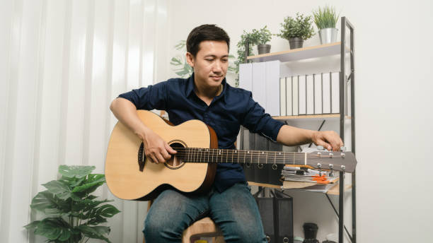 istock Young joyful asian handsome man playing  guitar at home. 1494250762