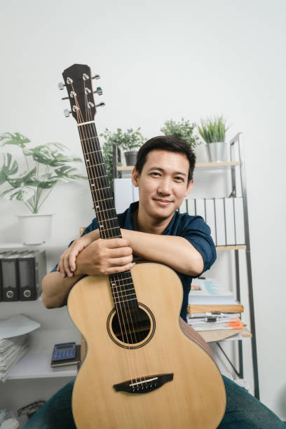 istock Young joyful asian handsome man playing  guitar at home. 1494250790