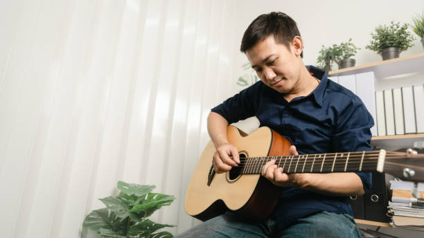 istock Young joyful asian handsome man playing  guitar at home. 1494250791