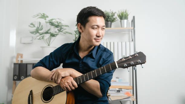 istock Young joyful asian handsome man playing  guitar at home. 1494250797