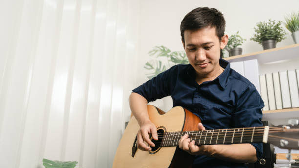 istock Young joyful asian handsome man playing  guitar at home. 1494250809