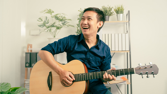 Young joyful asian handsome man playing  guitar at home.