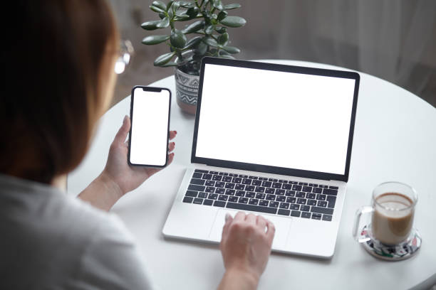istock Mockup white screen laptop and mobile phone woman using computer while sitting at table at home, back view 1494251816