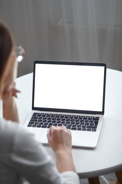 istock Mockup white screen laptop woman using computer while sitting at table at home, back view 1494251883