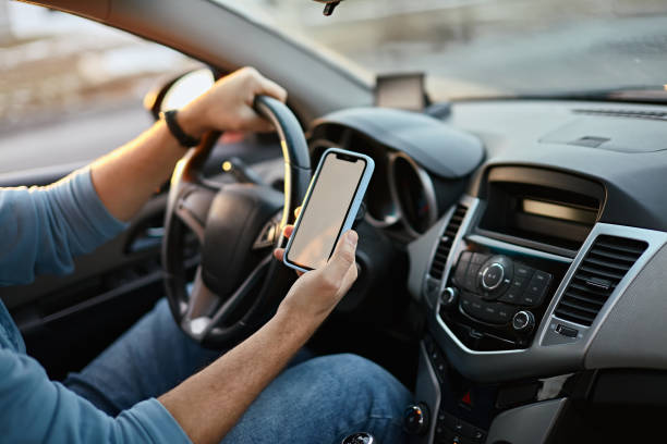 istock Hands of unrecognizable man driver using white screen mockup mobile phone while driving 1494251979