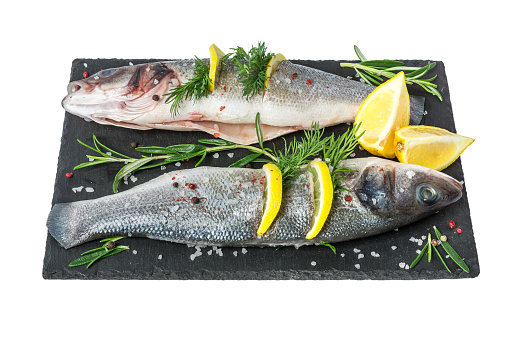 Fresh fish seabass and ingredients for cooking. Raw gutted fish sea bass with spices and herbs on black slate isolated on white background